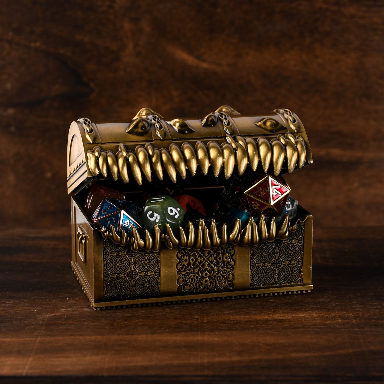 A gold-colored metal mimic chest filled with multicolored dice, set against a wooden background.