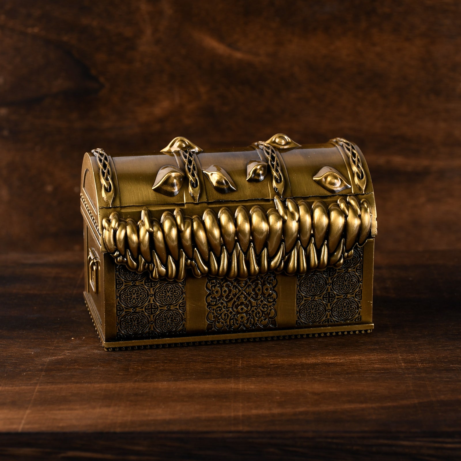 A gold-colored metal mimic chest filled with multicolored dice, set against a wooden background.