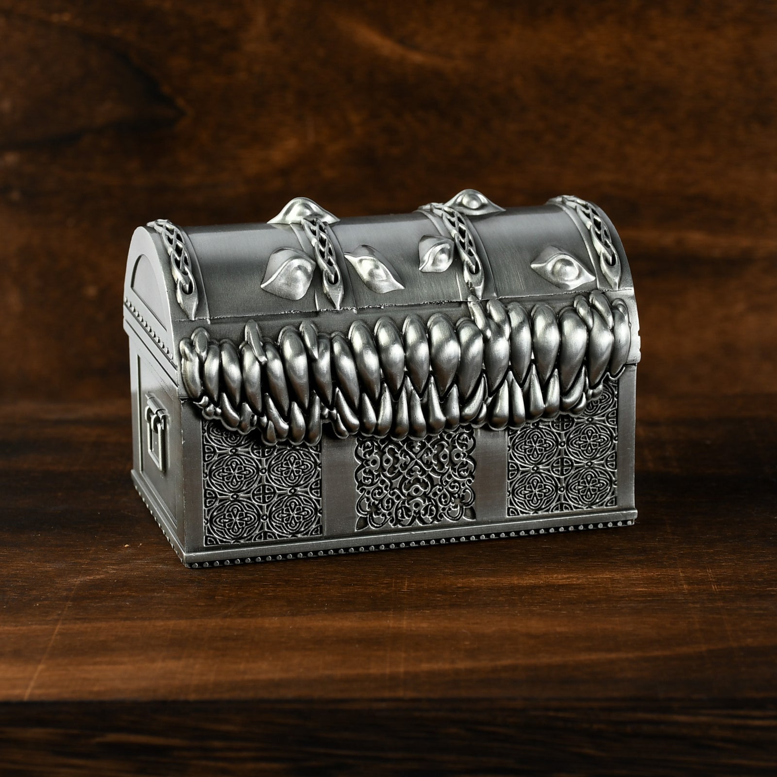 A silver metal chest designed to look like a mimic with teeth, open and filled with multicolored gaming dice.