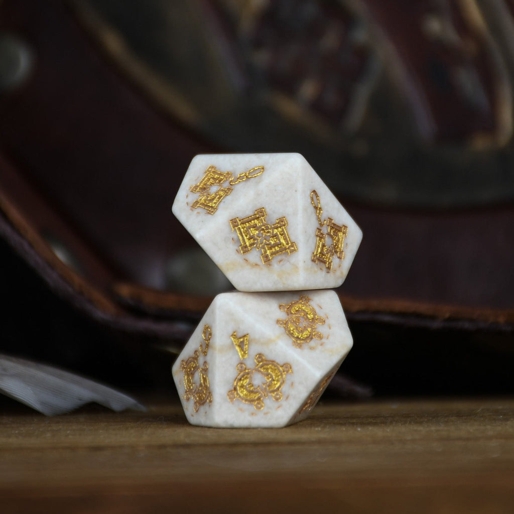 A set of hand-carved white opal stone dice with gold engravings, including various shapes typical for role-playing games like a d4, d6, d8, d10, d12, and d20. The dice are displayed on a wooden surface with a blurred background.