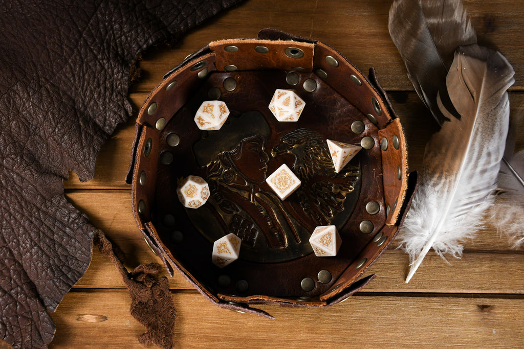 A set of hand-carved white opal stone dice with gold engravings, including various shapes typical for role-playing games like a d4, d6, d8, d10, d12, and d20. The dice are displayed on a wooden surface with a blurred background.