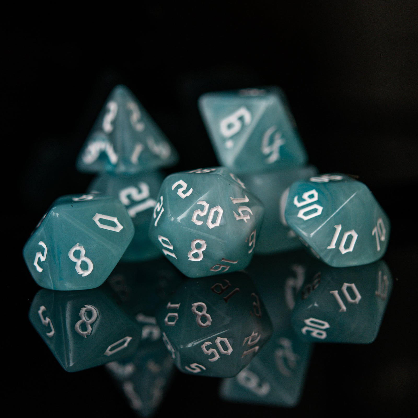 A set of teal blue acrylic dice with white numbers, including various shapes typical for role-playing games.