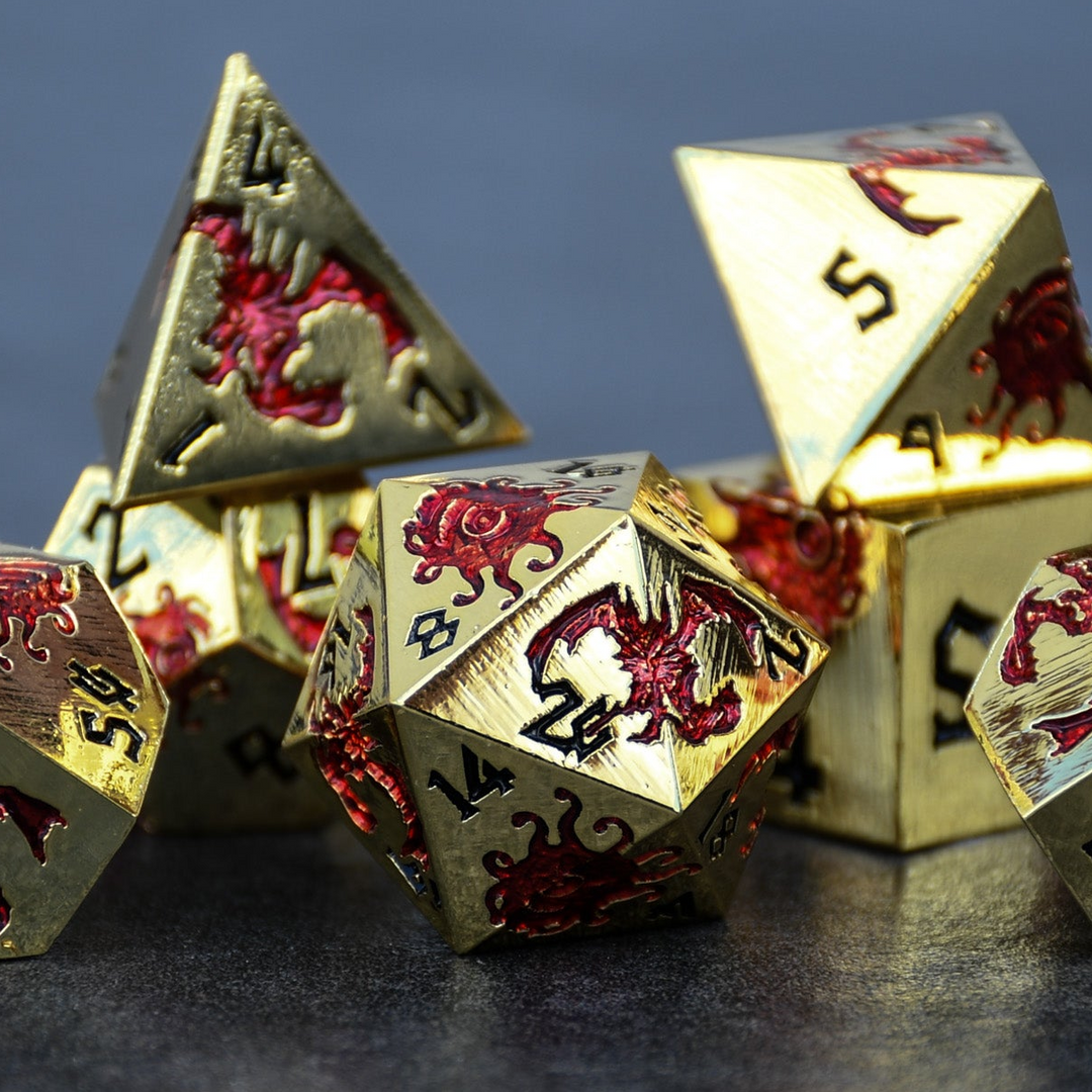 A set of gold metal polyhedral dice with red dnd monsters and black numbering for dnd and ttrpg