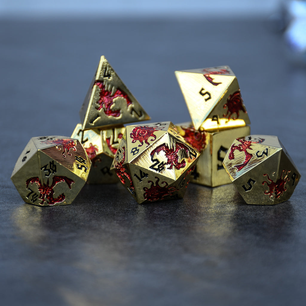 A set of gold metal polyhedral dice with red dnd monsters and black numbering for dnd and ttrpg