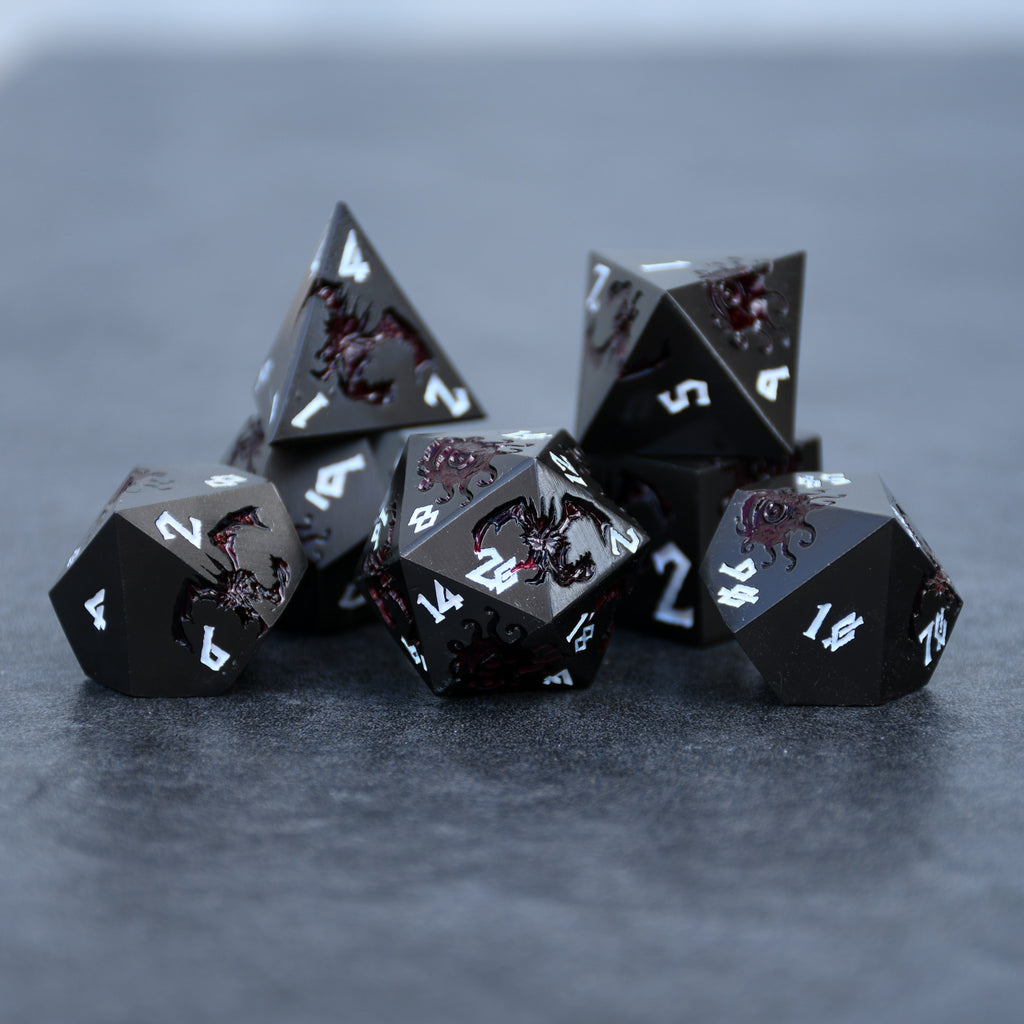 A set of metal dice in gunmetal and crimson color with engraved dragons and beholders in crimson read and white numbers 