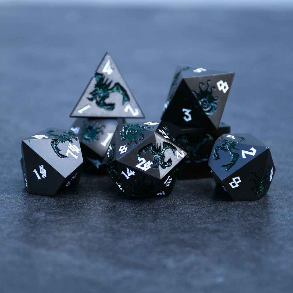 A set of metal dice in gunmetal and green color with engraved numbers, including various shapes such as a d4, d6, d8, d10, d12, and d20, displayed on a dark surface.