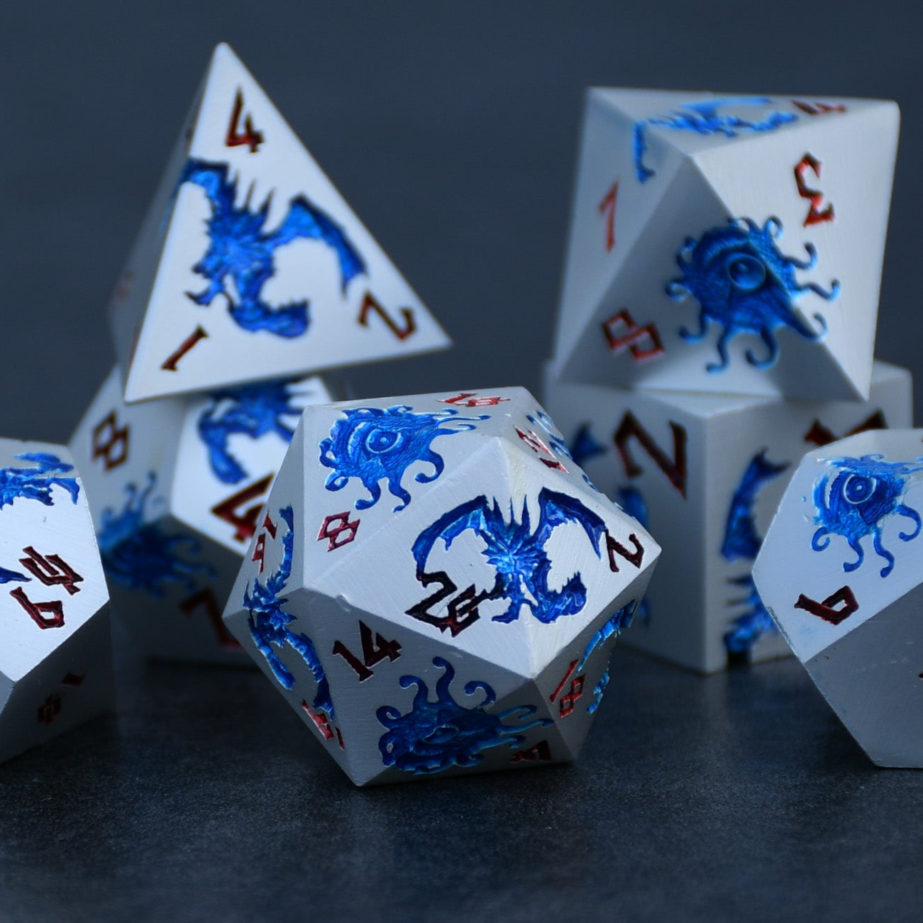 A set of silver metal dnd dice with blue monster patterns on them and red numbering