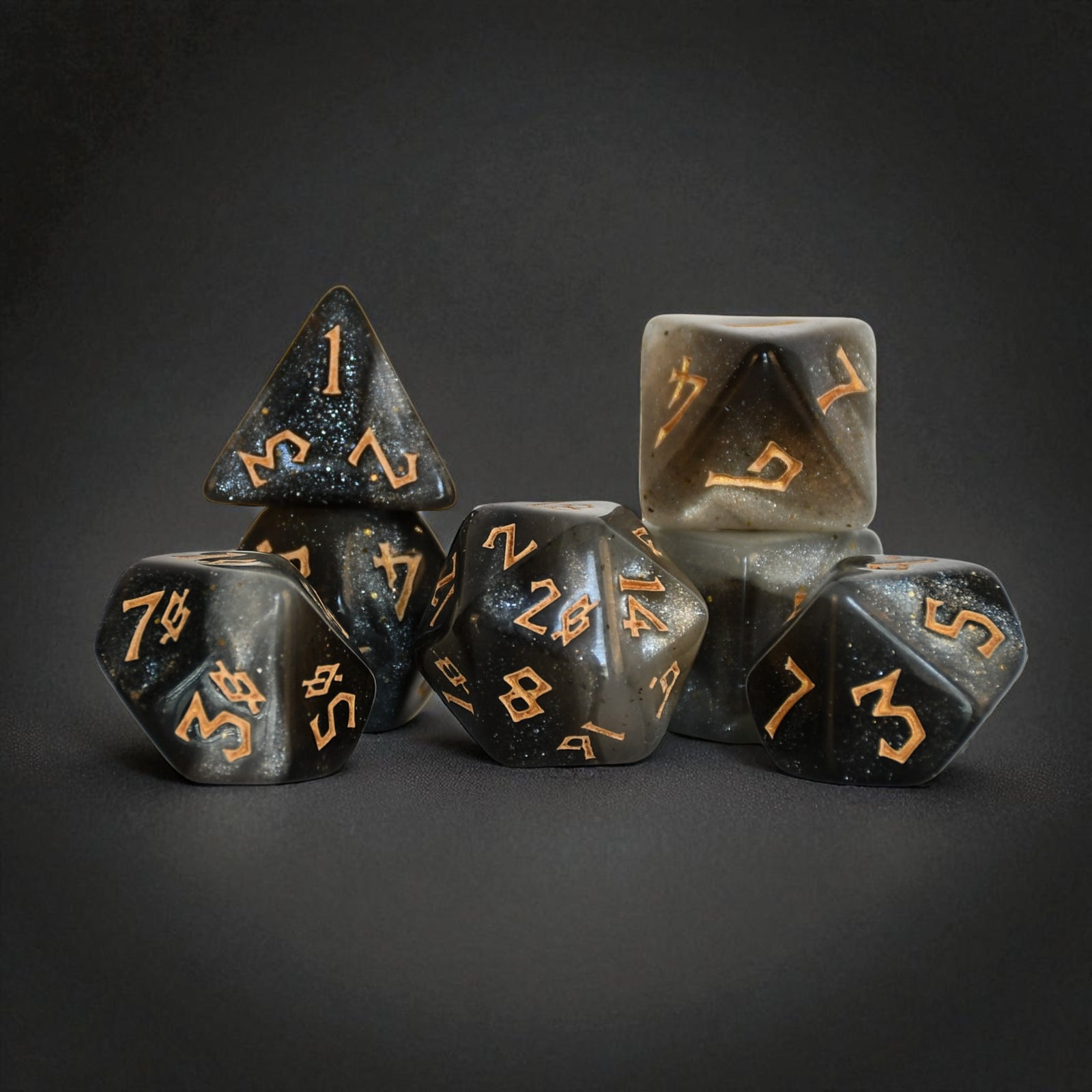 Set of dark gray polyhedral dice with gold numbering on a black background