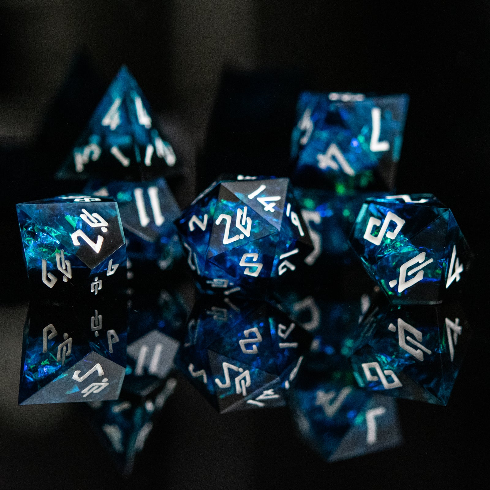 A set of sharp-edged, blue resin dice with engraved numbers, reflecting on a black surface.