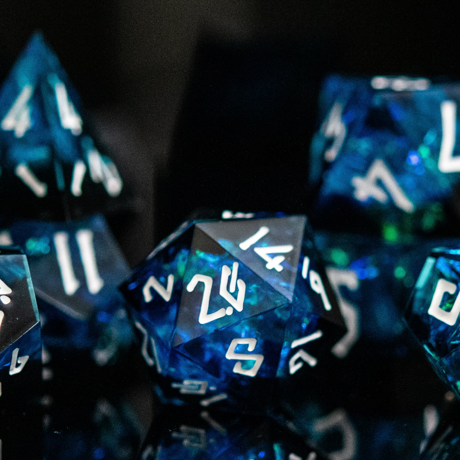 A set of sharp-edged, blue resin dice with engraved numbers, reflecting on a black surface.