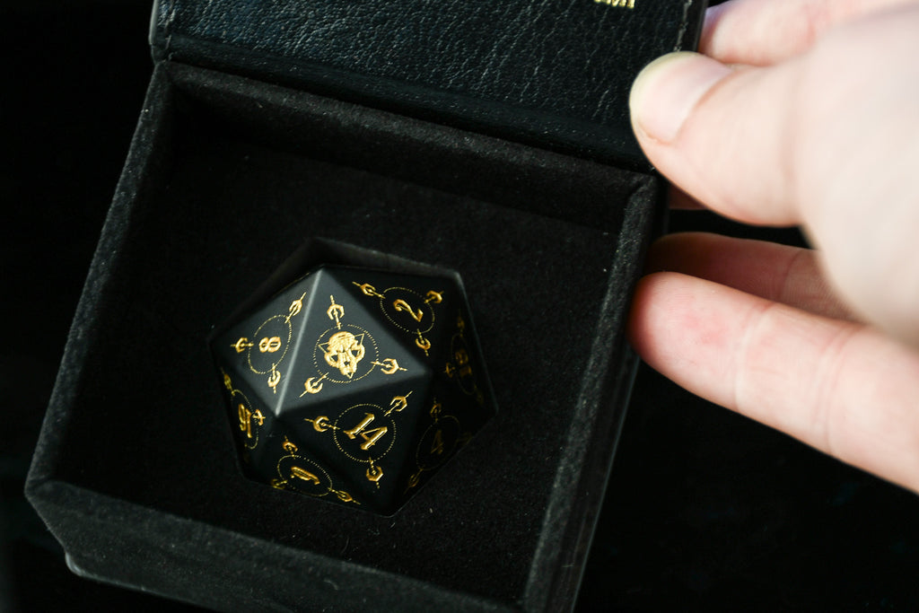 Black polyhedral dice with gold numbering held in a black velvet box.