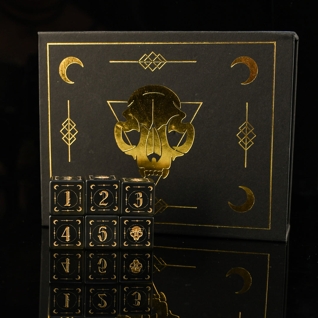 Black box with gold skull and number design on a black background and 6 d6 dice in black frosted glass with golden font, creasant moons and adornments 