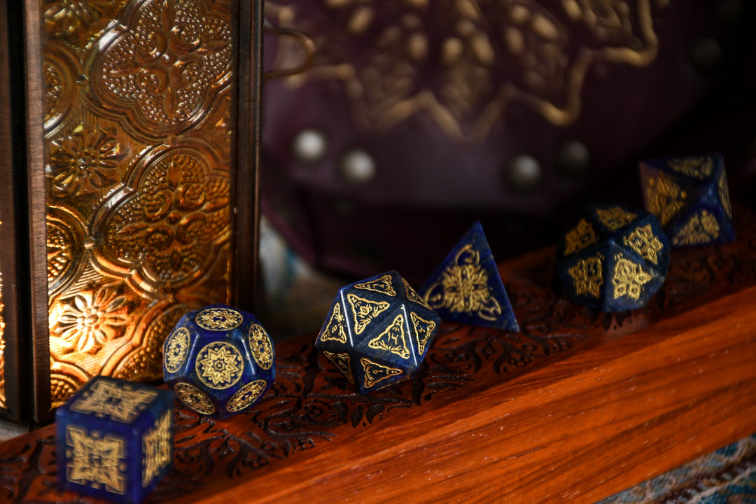 A set of hand-carved blue lapis stone dice with golden patterns, displayed on a wooden dnd dice vault