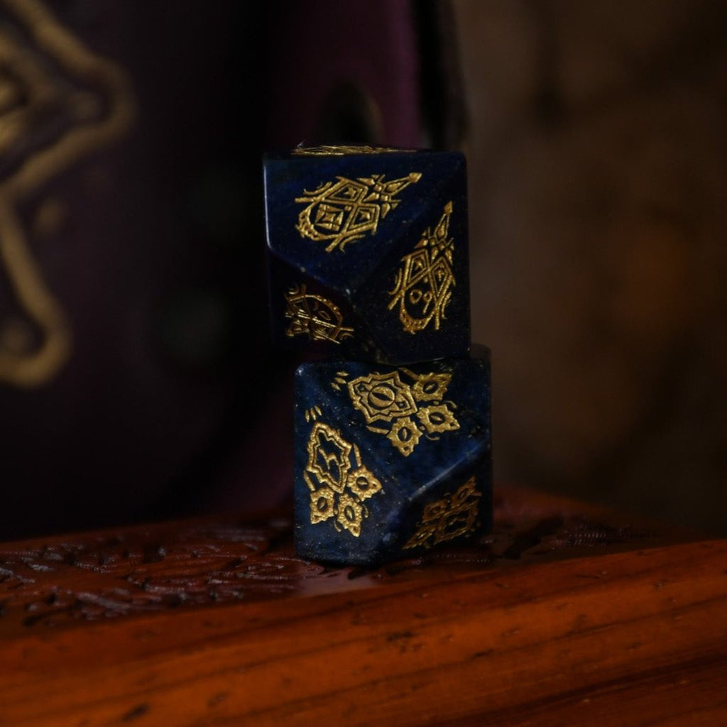 A set of hand-carved blue lapis stone dice with golden patterns, displayed on a wooden surface.