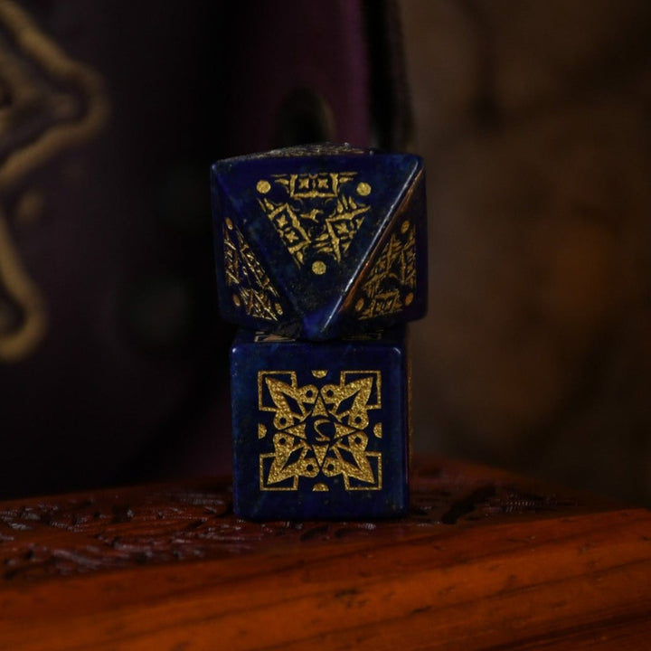 A set of hand-carved blue lapis stone dice with golden patterns, displayed on a wooden surface.