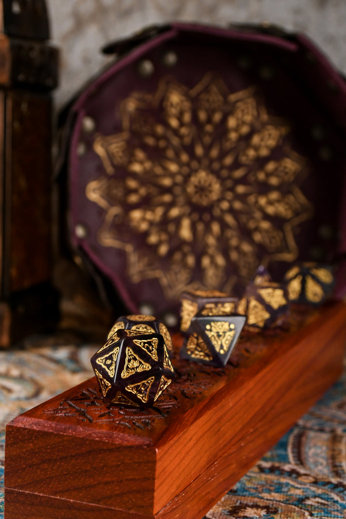 A set of purple fluorite stone dice with gold engravings, displayed on a wooden dnd dice vault.