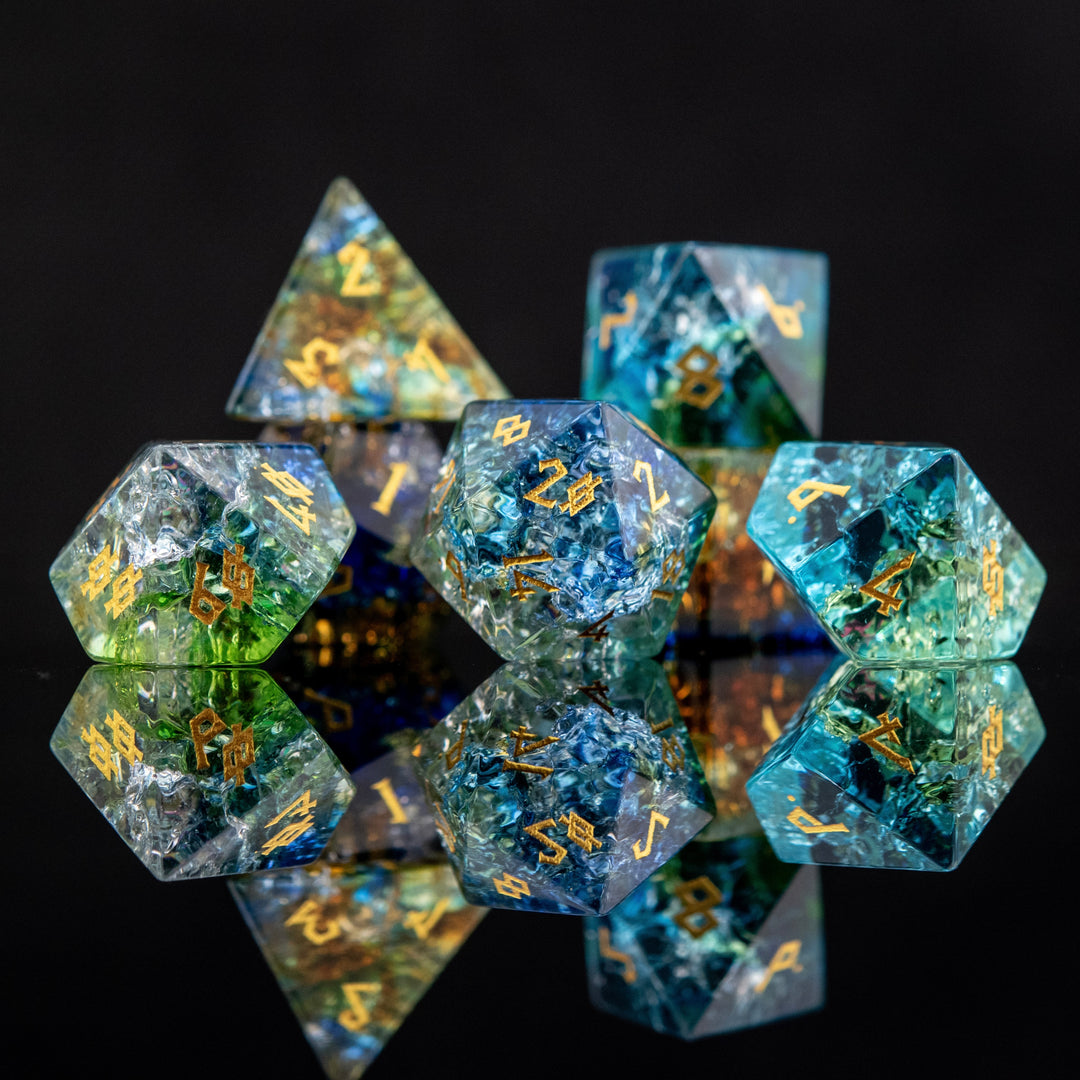 A set of shattered glass dice with engraved numbers, featuring a variety of colors including blue, green, and orange, displayed on a reflective surface.
