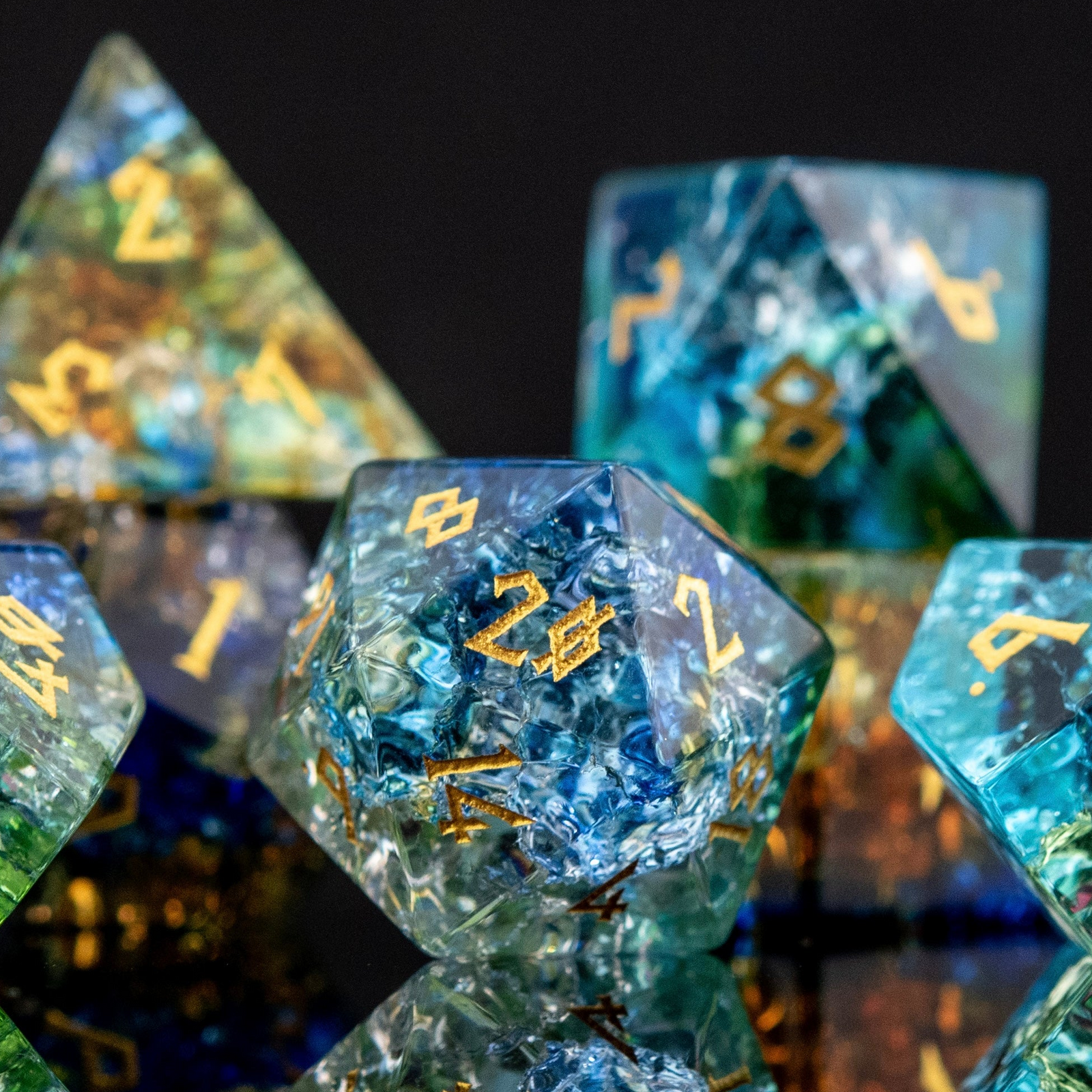 A set of shattered glass dice with engraved numbers, featuring a variety of colors including blue, green, and orange, displayed on a reflective surface.