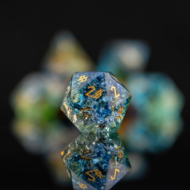 A set of shattered glass dice with engraved numbers, featuring a variety of colors including blue, green, and orange, displayed on a reflective surface.