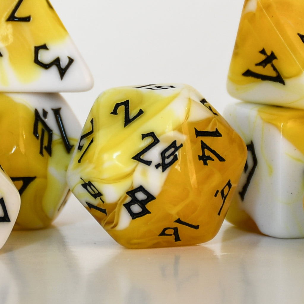 Close-up of yellow and white polyhedral acrylic dnd dice with black numbers on a reflective surface.