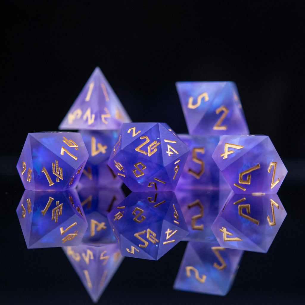 A set of matte purple sharp-edged resin dnd dice with gold engraved numbers, reflecting on a black surface.