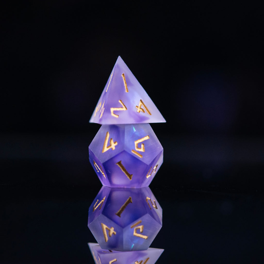 A set of matte purple sharp-edged resin dnd dice with gold engraved numbers, reflecting on a black surface.