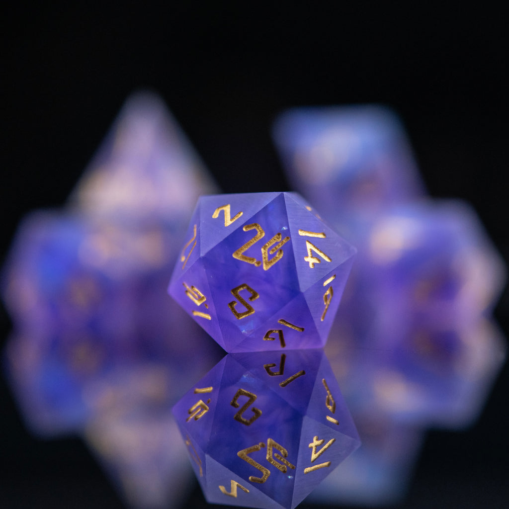 A set of matte purple sharp-edged resin dnd dice with gold engraved numbers, reflecting on a black surface.