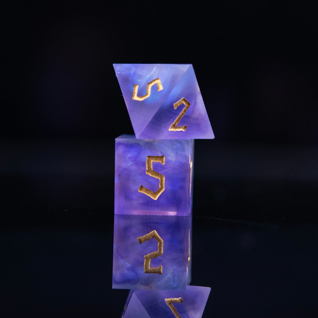 A set of matte purple sharp-edged resin dnd dice with gold engraved numbers, reflecting on a black surface.