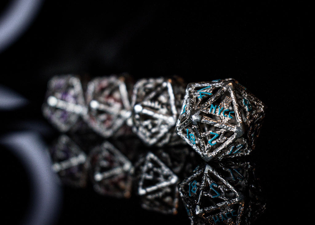 A set of sterling silver hollow dice with embossed numbers, displayed on a reflective surface.