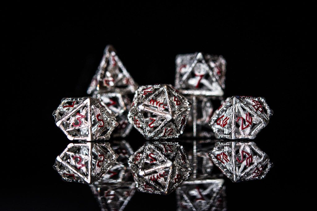 A set of sterling silver dice with red embossed numbers, displayed on a reflective surface.