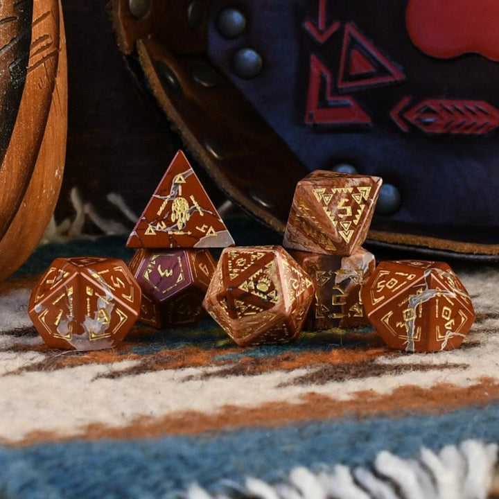A set of hand-carved red jasper stone dice with intricate engravings, displayed on a patterned fabric.