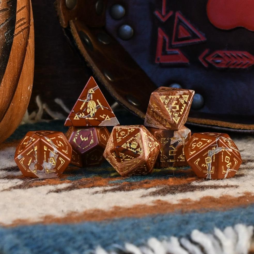 A set of hand-carved red jasper stone dice with intricate engravings, displayed on a patterned fabric.
