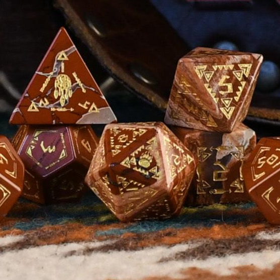 A set of hand-carved red jasper stone dice with intricate engravings, displayed on a patterned fabric.