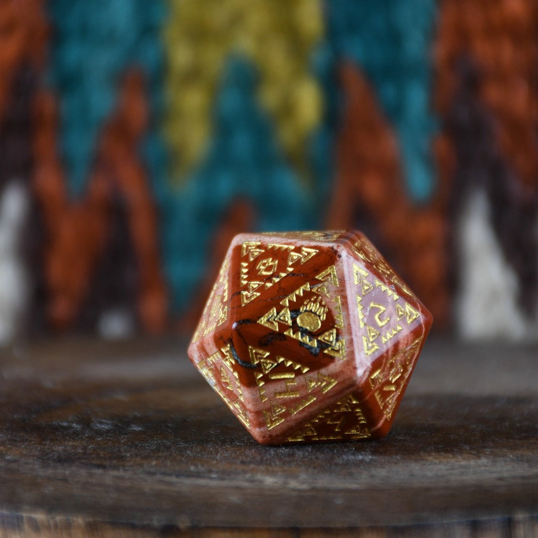 A set of hand-carved red jasper stone dice with intricate engravings, displayed on a patterned fabric.