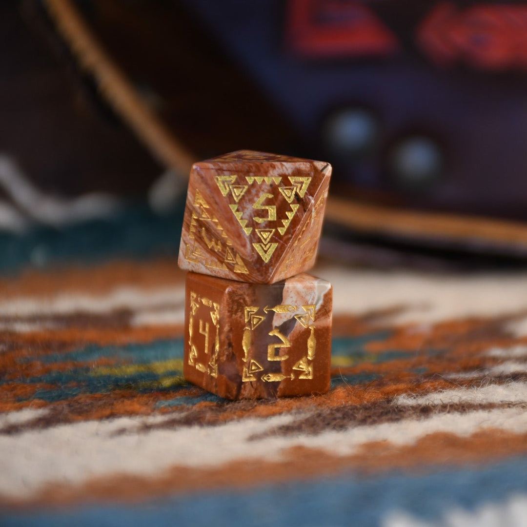 A set of hand-carved red jasper stone dice with intricate engravings, displayed on a patterned fabric.