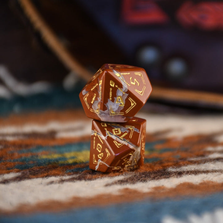 A set of hand-carved red jasper stone dice with intricate engravings, displayed on a patterned fabric.
