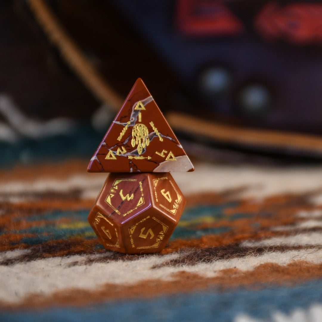 A set of hand-carved red jasper stone dice with intricate engravings, displayed on a patterned fabric.
