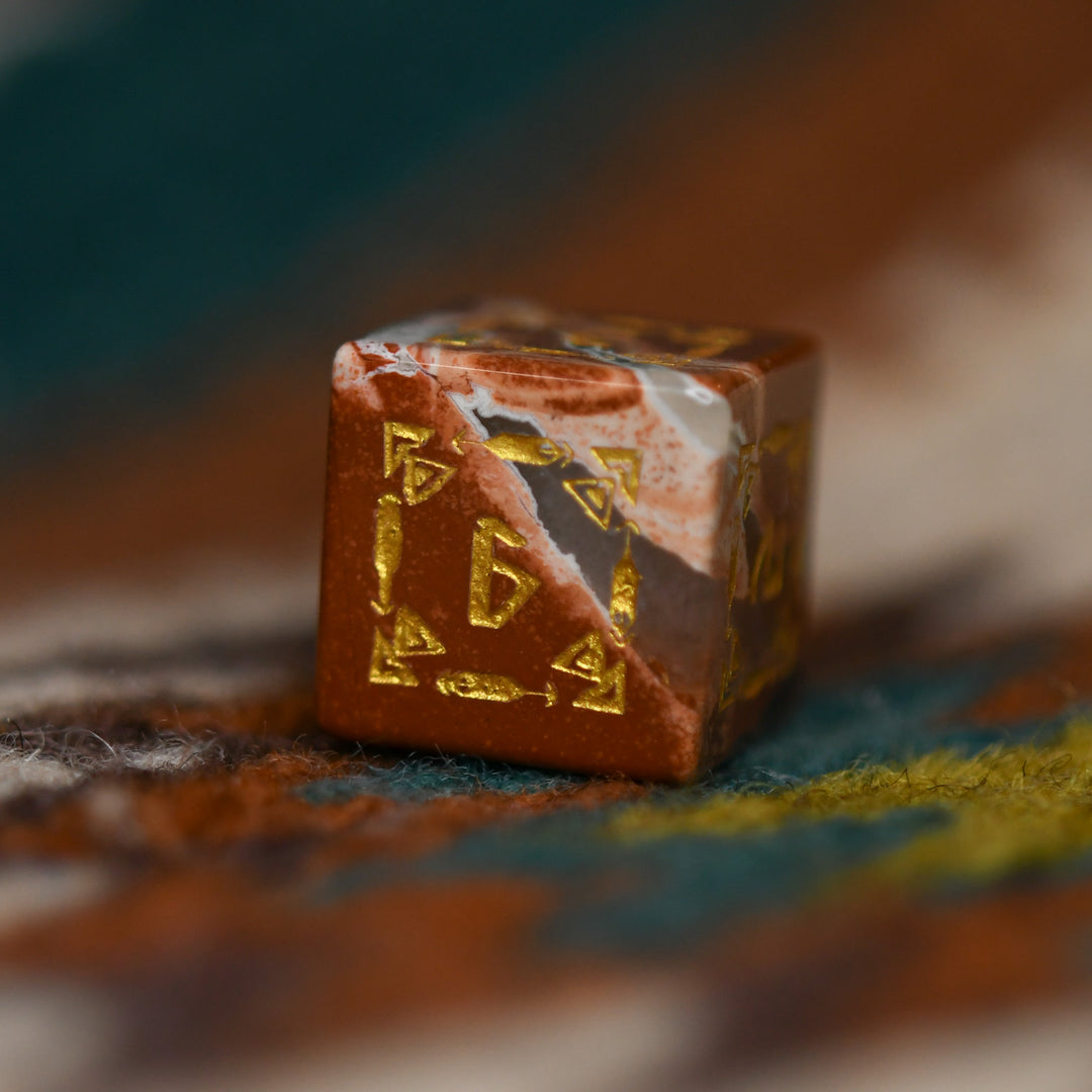 A set of hand-carved red jasper stone dice with intricate engravings, displayed on a patterned fabric.