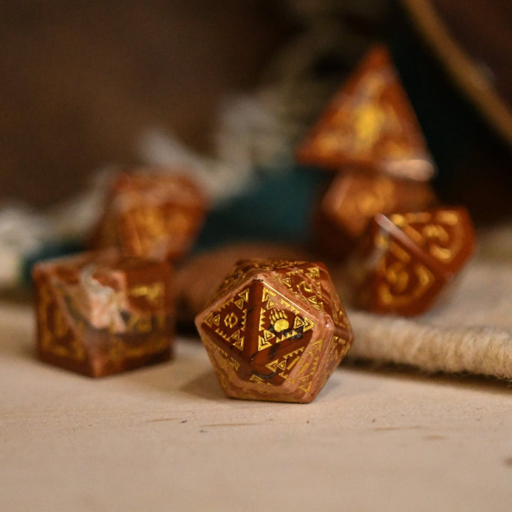 A set of hand-carved red jasper stone dice with intricate engravings, displayed on a patterned fabric.