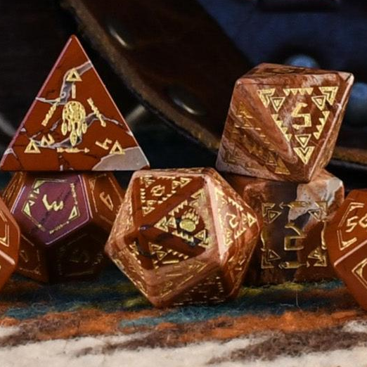 A set of hand-carved red jasper stone dice with intricate engravings, displayed on a patterned fabric.