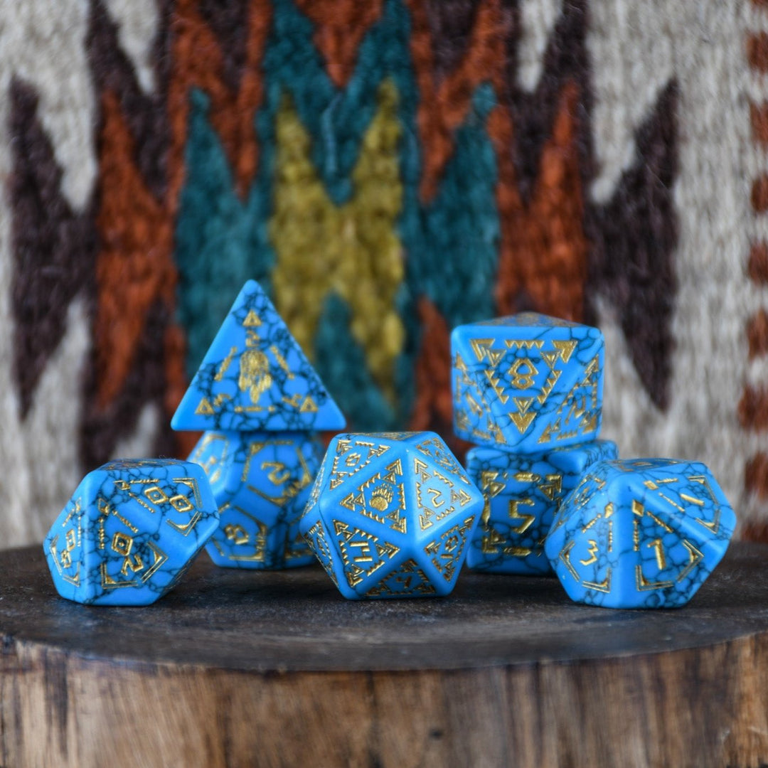 A set of hand-carved blue turquoise stone dice with gold patterns, displayed on a wooden surface against an embroidered background.