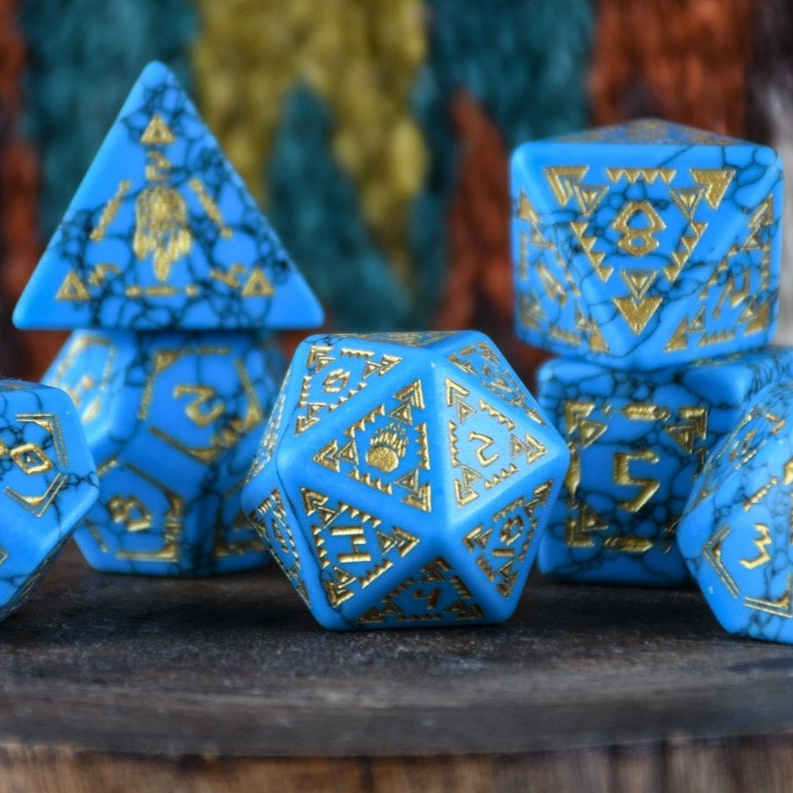 Blue polyhedral dice with gold patterns on a wooden surface
