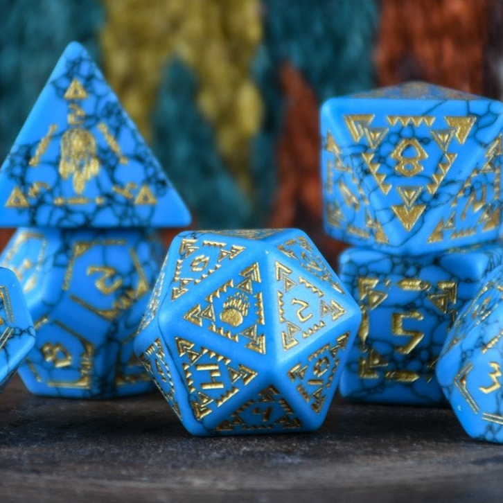 A set of hand-carved blue turquoise stone dice with gold patterns, displayed on a wooden surface against an embroidered background.