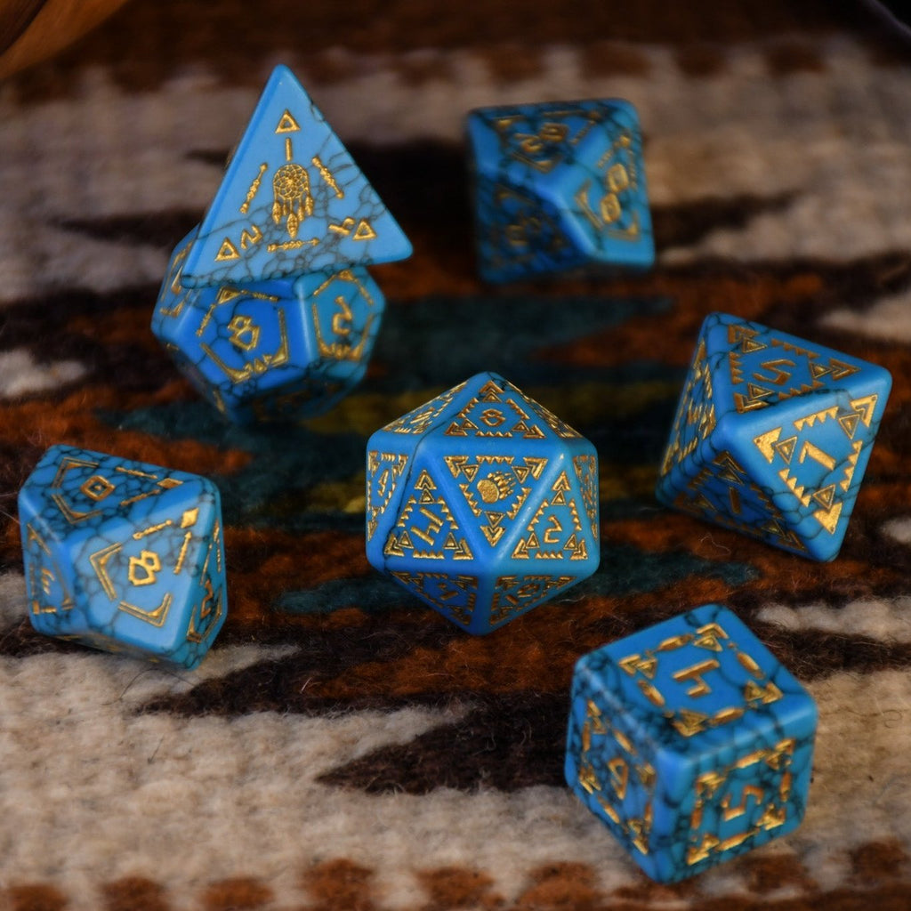 A set of hand-carved blue turquoise stone dice with gold patterns, displayed on a wooden surface against an embroidered background.