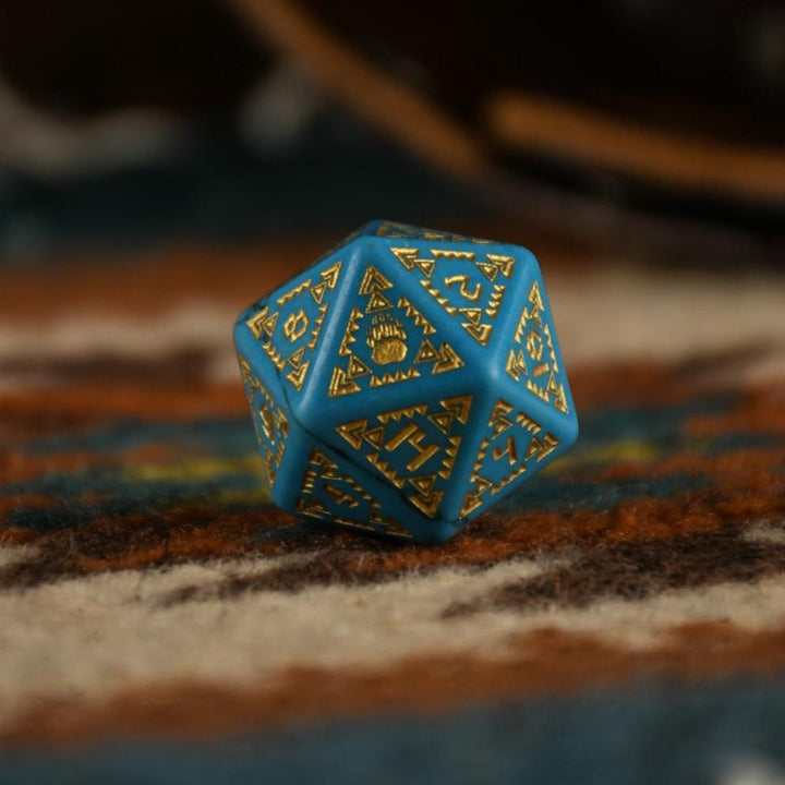 A set of hand-carved blue turquoise stone dice with gold patterns, displayed on a wooden surface against an embroidered background.