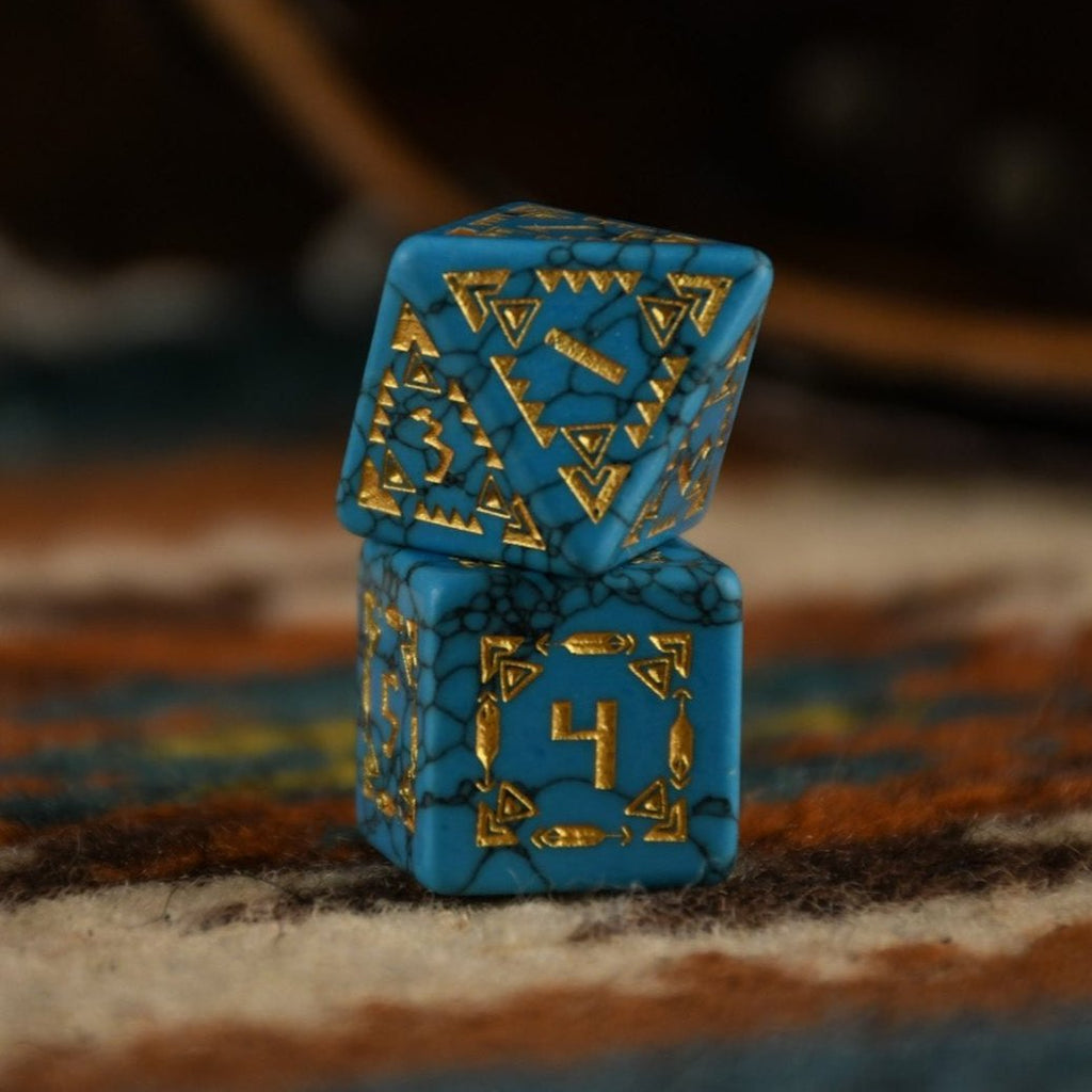 A set of hand-carved blue turquoise stone dice with gold patterns, displayed on a wooden surface against an embroidered background.