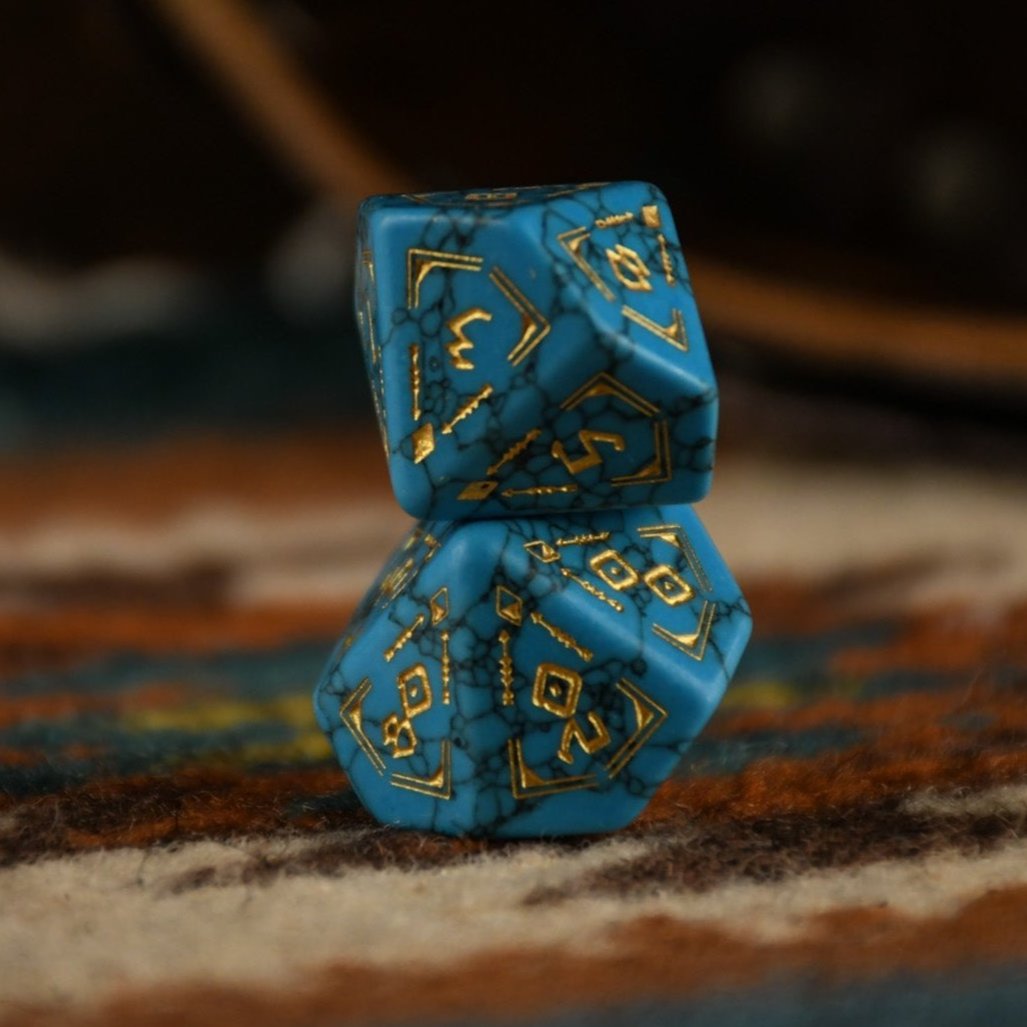 A set of hand-carved blue turquoise stone dice with gold patterns, displayed on a wooden surface against an embroidered background.