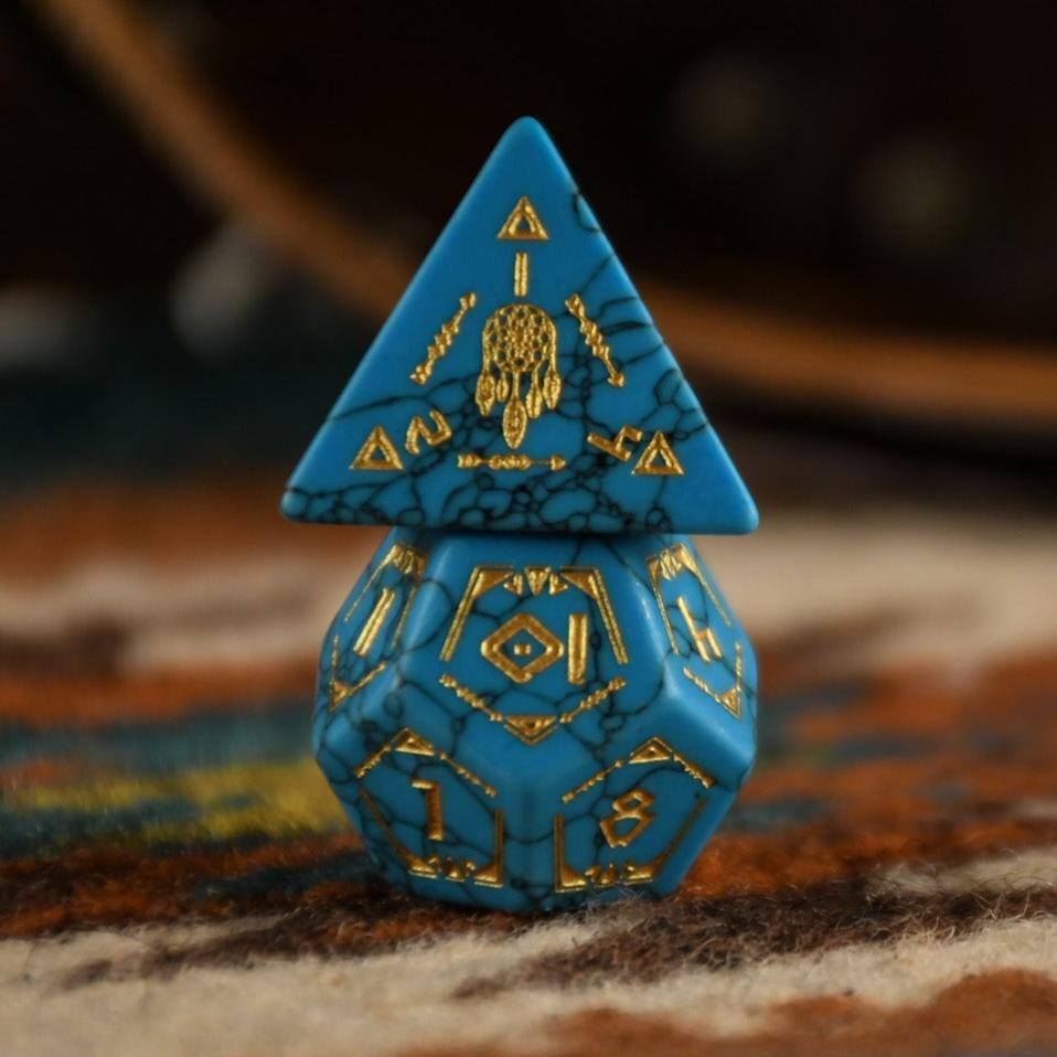 A set of hand-carved blue turquoise stone dice with gold patterns, displayed on a wooden surface against an embroidered background.