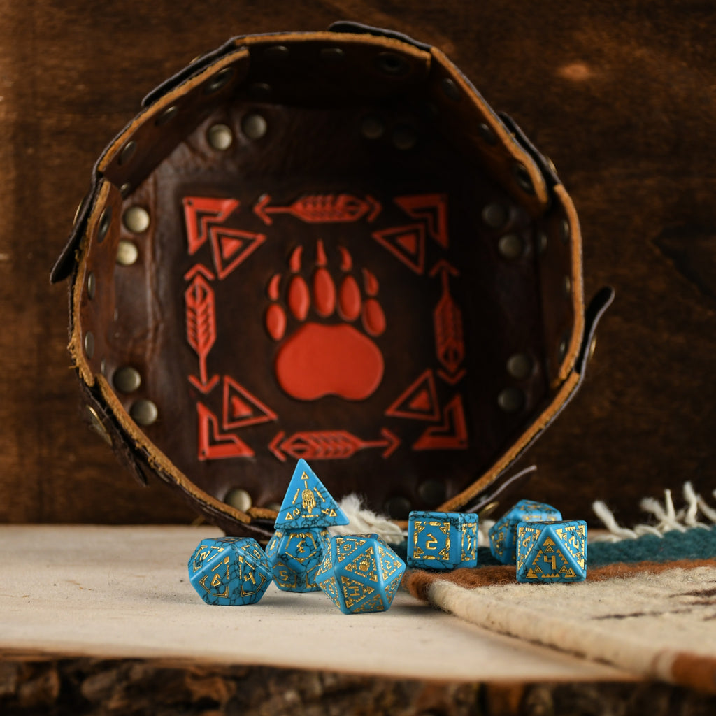 A set of hand-carved blue turquoise stone dice with gold patterns, displayed on a wooden surface against an embroidered background.