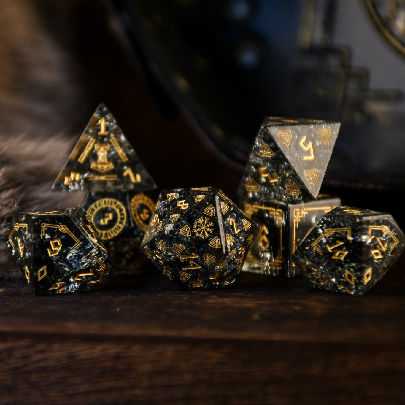 A set of black shattered glass polyhedral dice with Nordic designs, including one d4, one d6, one d8, two d10, one d12, and one d20, displayed on a wooden surface.